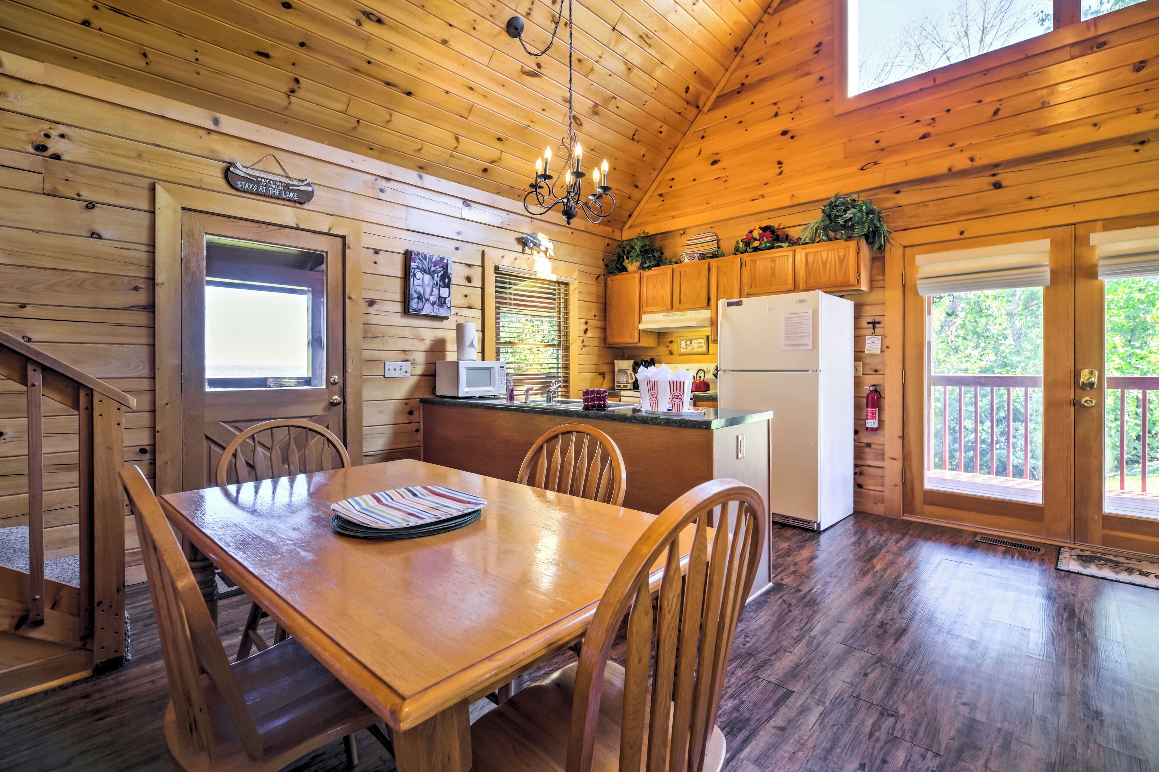 A wooden cabin interior with a dining table, chairs, a kitchen area, and a staircase.