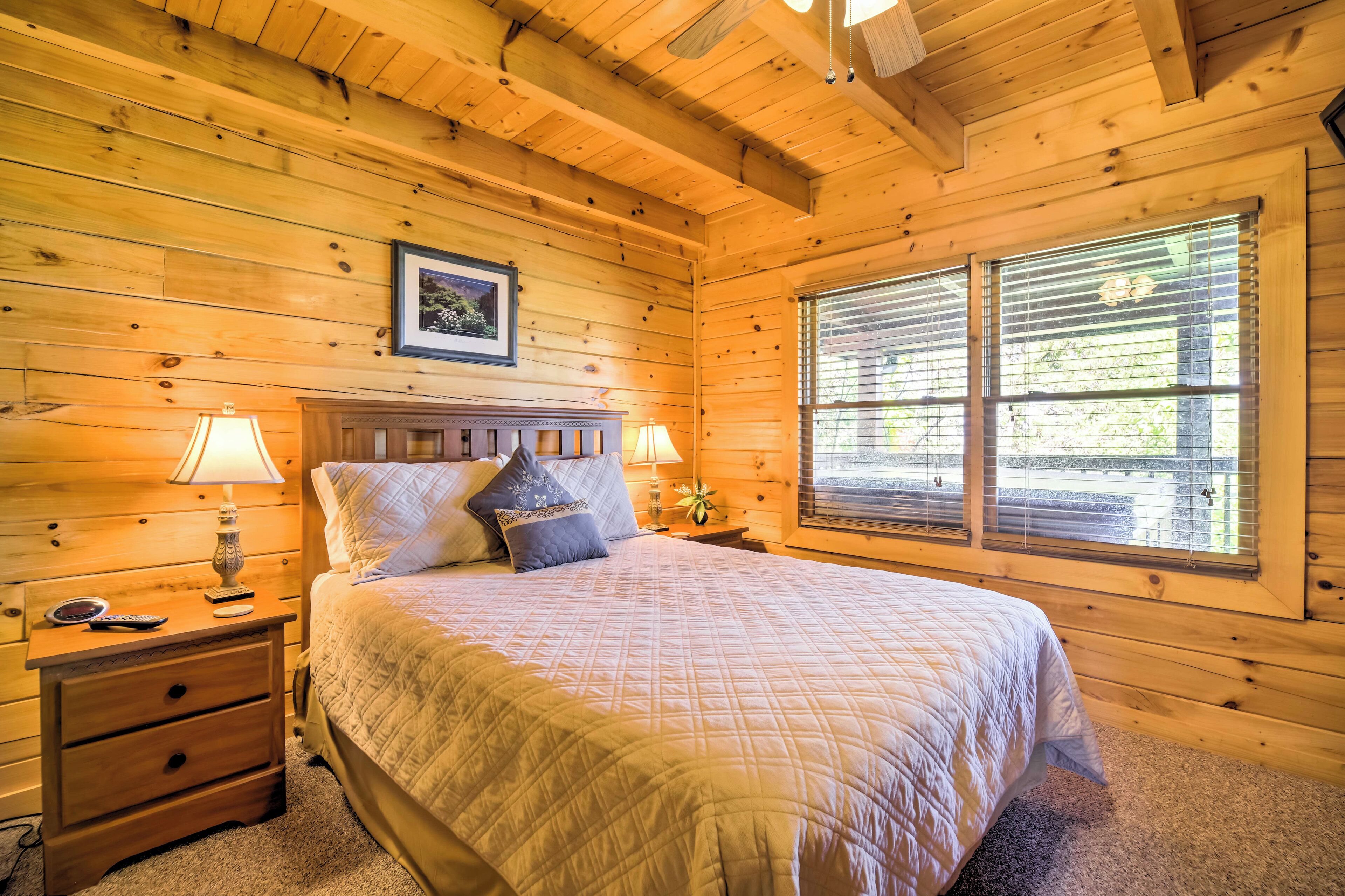 Ein Schlafzimmer einer Holzhütte mit einem Bett, zwei Nachttischen, einem Beistelltisch, einer Lampe und einem Fenster mit Jalousien.