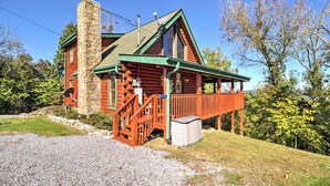A log cabin with a stone chimney, a wooden deck, and a stone foundation.