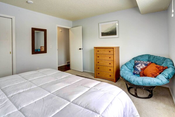 A bedroom with a large bed, a wooden dresser, a chair, and a door leading to another room.
