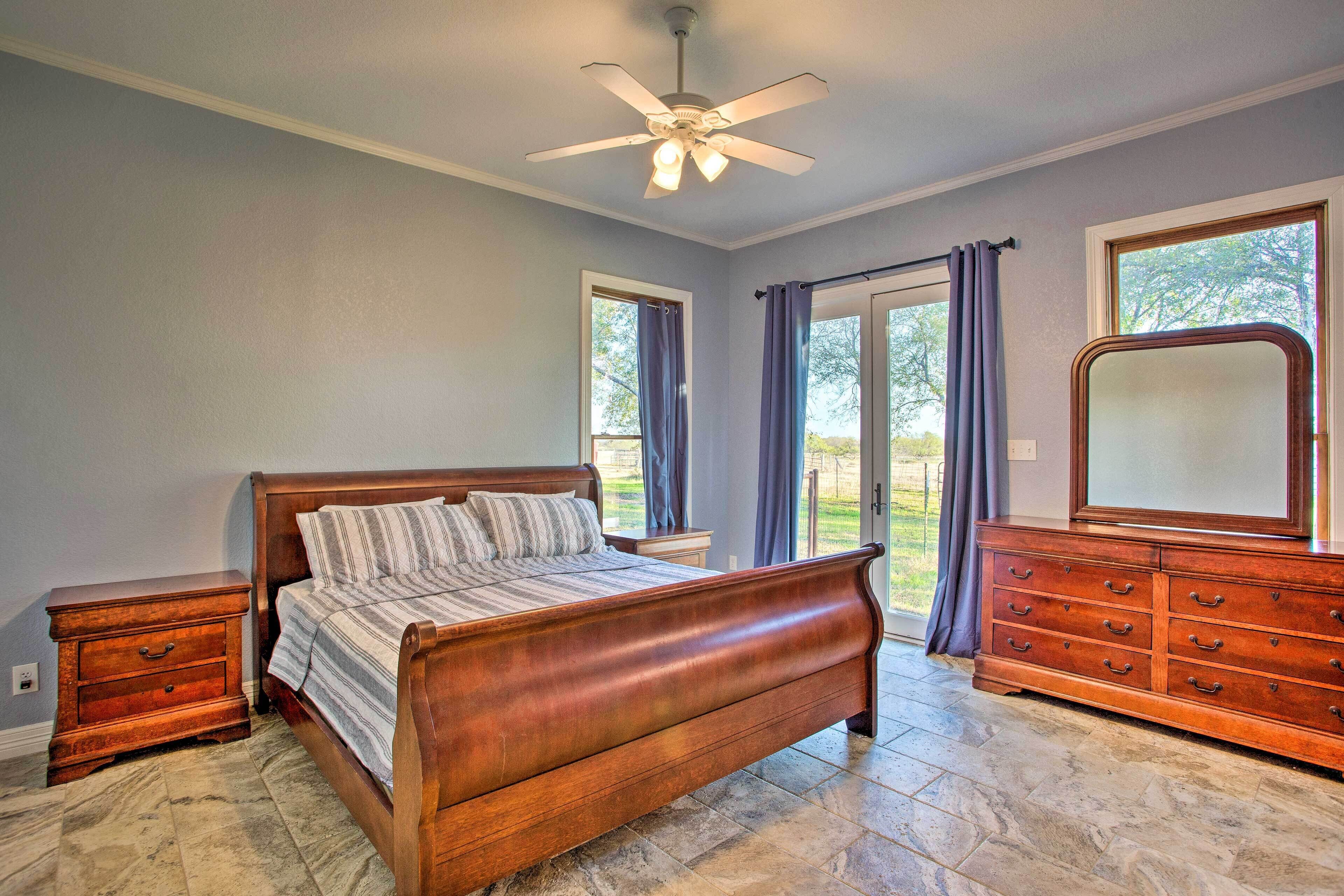A bedroom with a wooden bed, a dresser, a ceiling fan, and a large window with curtains.