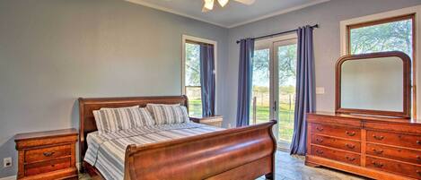 A bedroom with a wooden bed, a dresser, a ceiling fan, and a large window with curtains.