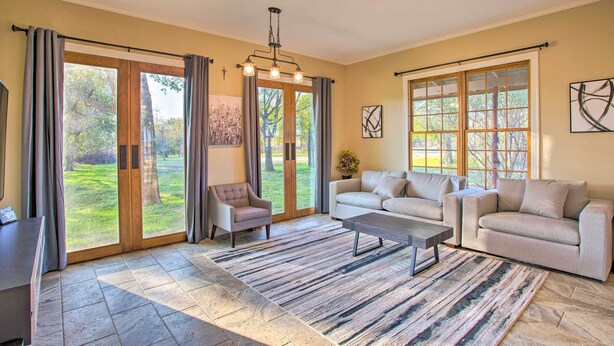 A spacious living room with a large sliding glass door leading to a garden, a sofa set, a coffee table, and a chandelier.