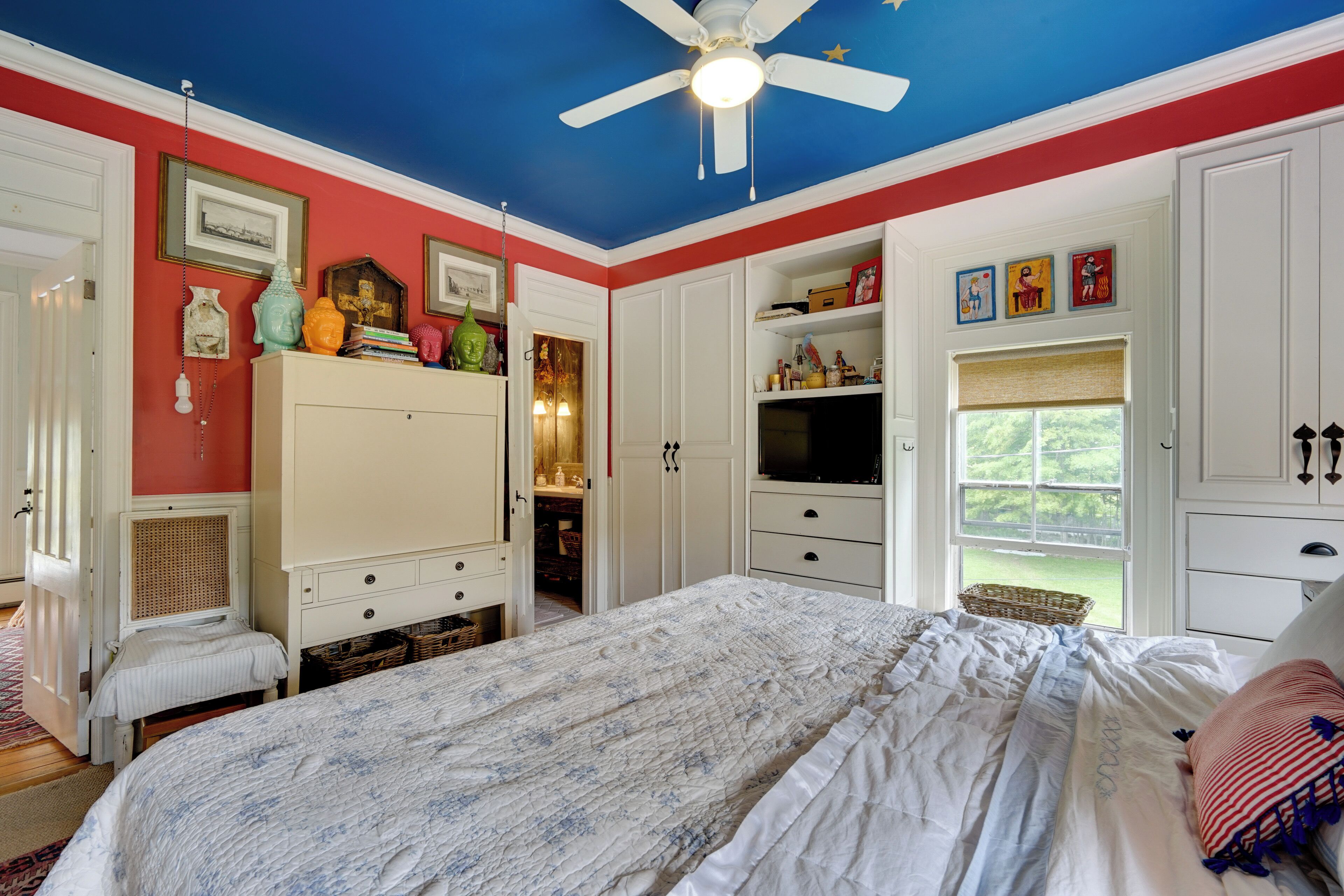 A bedroom with a bed, a ceiling fan, a television, and a window with a view.