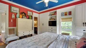 A bedroom with a bed, a ceiling fan, a television, and a window with a view.