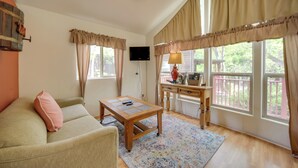 A cozy living room with a sofa, a coffee table, a desk with a lamp, and large windows with curtains. - Cozy Fredericksburg Cabin With Shared Hot Tub! (Fredericksburg)