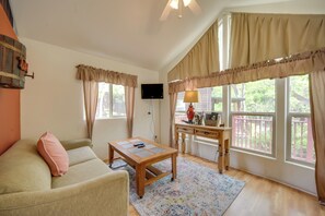 A cozy living room with a sofa, a coffee table, a desk with a lamp, and large windows with curtains. - Cozy Fredericksburg Cabin With Shared Hot Tub! (Fredericksburg)