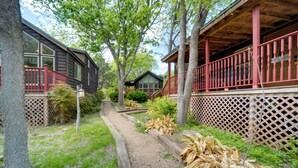 A pathway leading to a wooden cabin with a red railing and lattice fence. - Cozy Fredericksburg Cabin With Shared Hot Tub! (Fredericksburg)