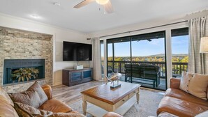 A spacious living room with leather sofas, a wooden coffee table, a fireplace, and a large sliding glass door leading to an outdoor balcony with a scenic view. - Hot Springs Vacation Rental w/ Game Room! (Hot Springs)