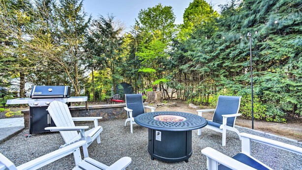 An outdoor patio area with Adirondack chairs, a round table, and a grill.