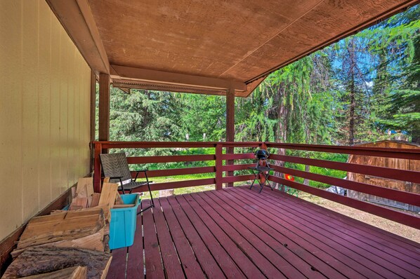A covered wooden deck with a view of a forest.