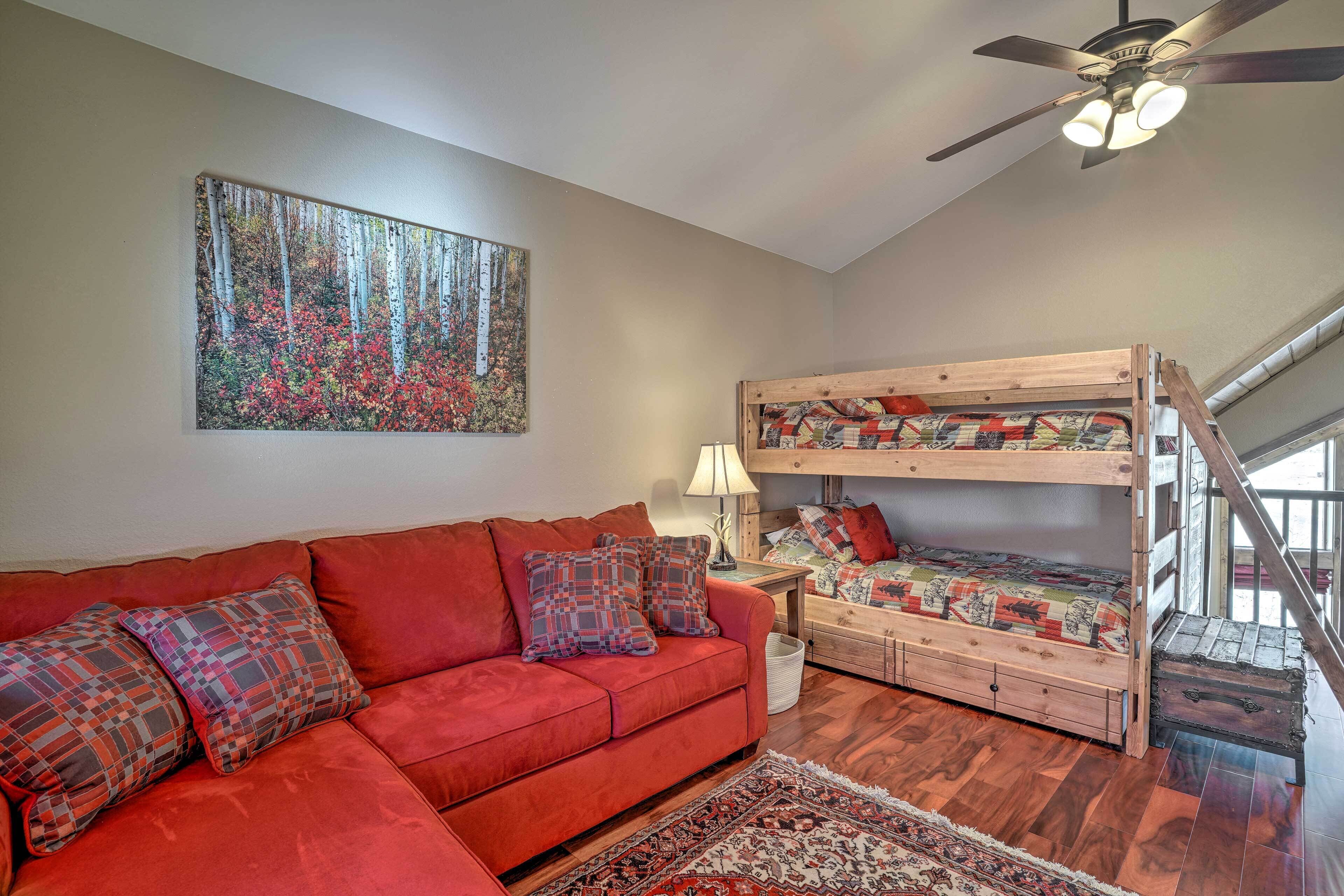 A room with a red sofa, a bunk bed, a ceiling fan, and a painting of a forest.