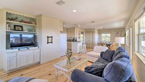 A spacious living area with a television, white cabinetry, a glass coffee table, and a grey sofa. - Gulf Shores Rental w/ Large Porch - Beach View! (Gulf Shores)