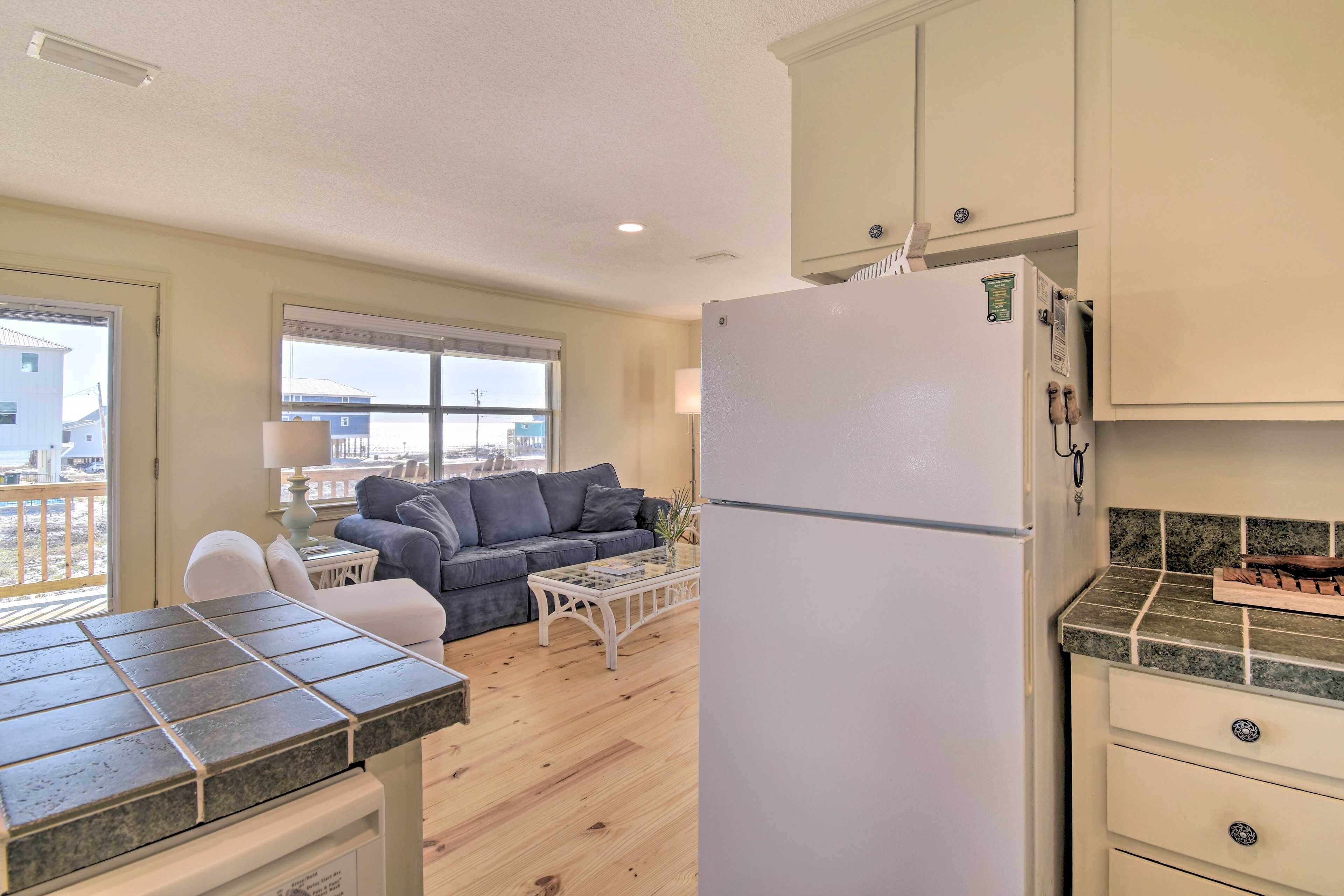 A kitchen with a refrigerator, a dining table with a tiled top, and a sofa in the background.
