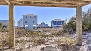 A wooden deck leading to a beach area with houses in the background. - Gulf Shores Rental w/ Large Porch - Beach View! (Gulf Shores)
