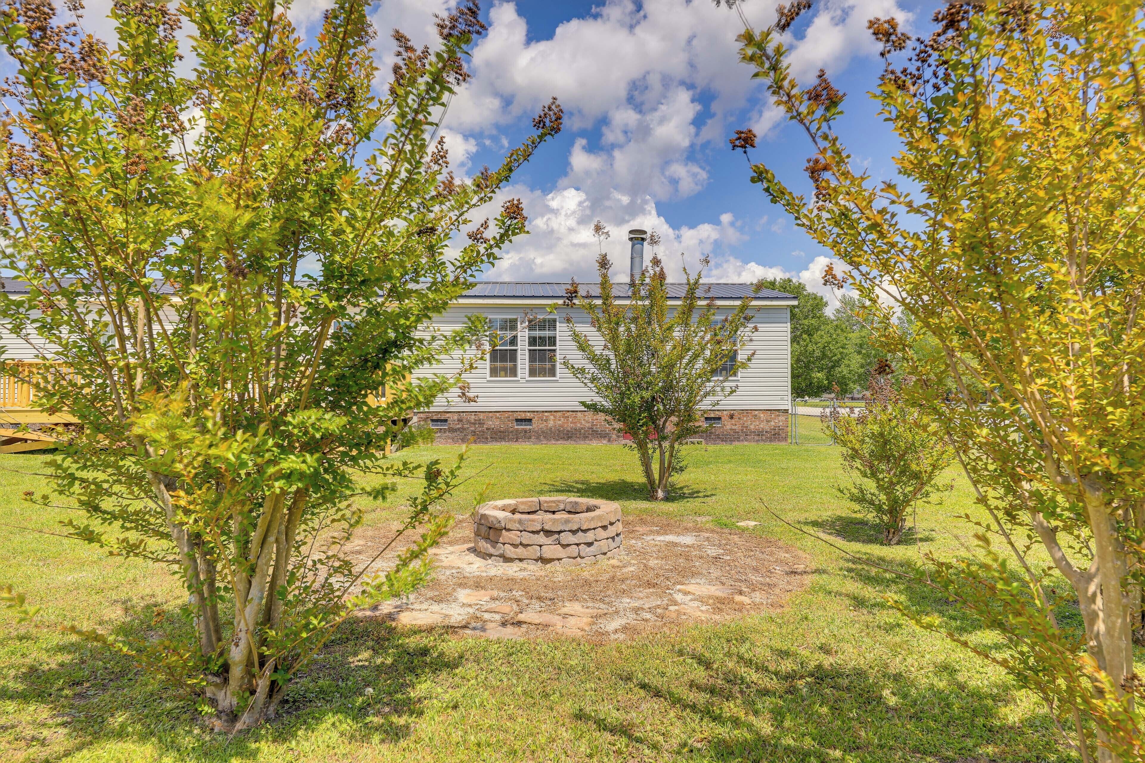 A grassy yard with a stone fire pit, a small tree, and a house with a chimney in the background.