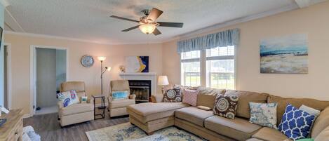 A living room with a sectional sofa, a chaise lounge, a fireplace, and a ceiling fan.