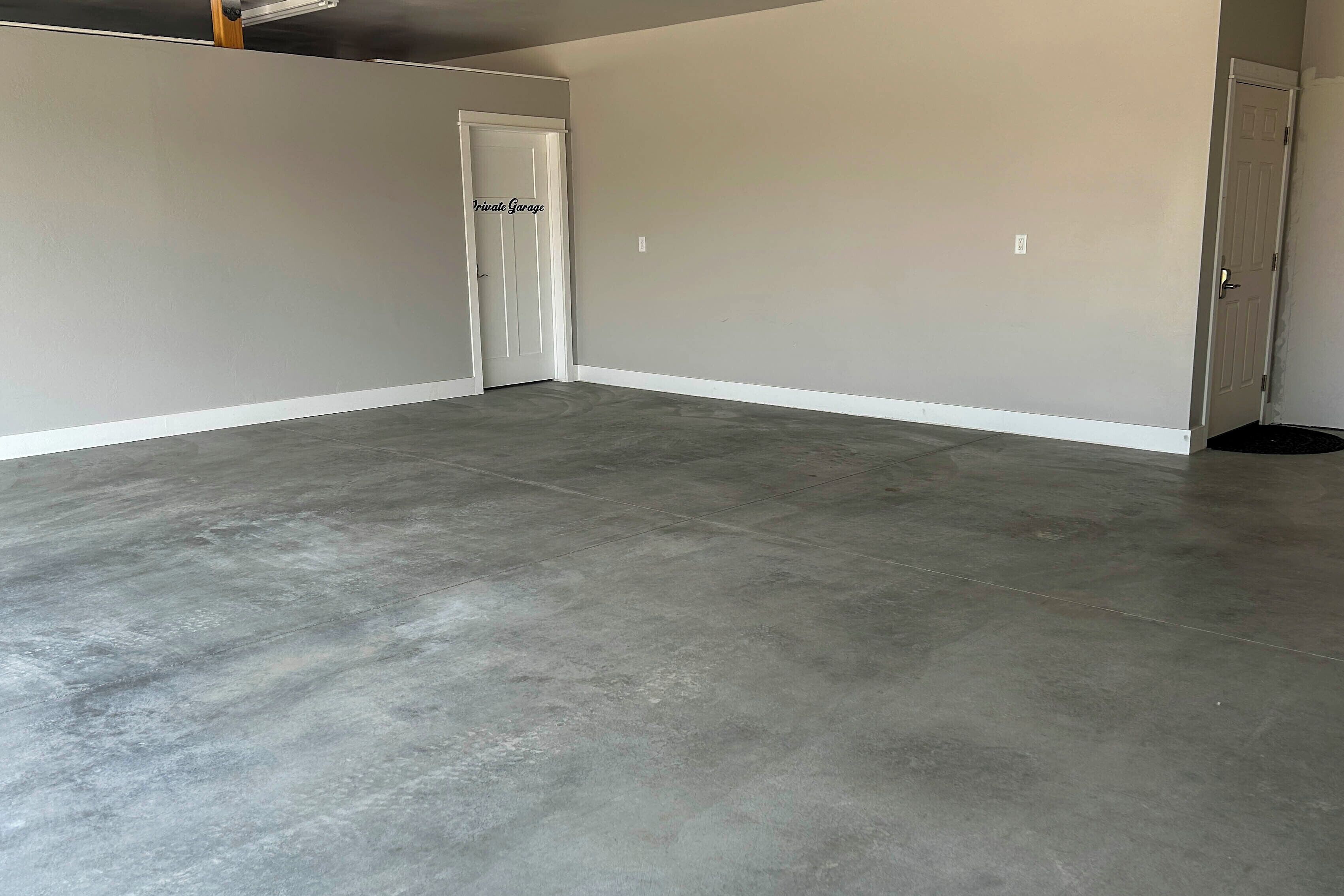 A spacious room with a grey concrete floor, white walls, and a closed door.