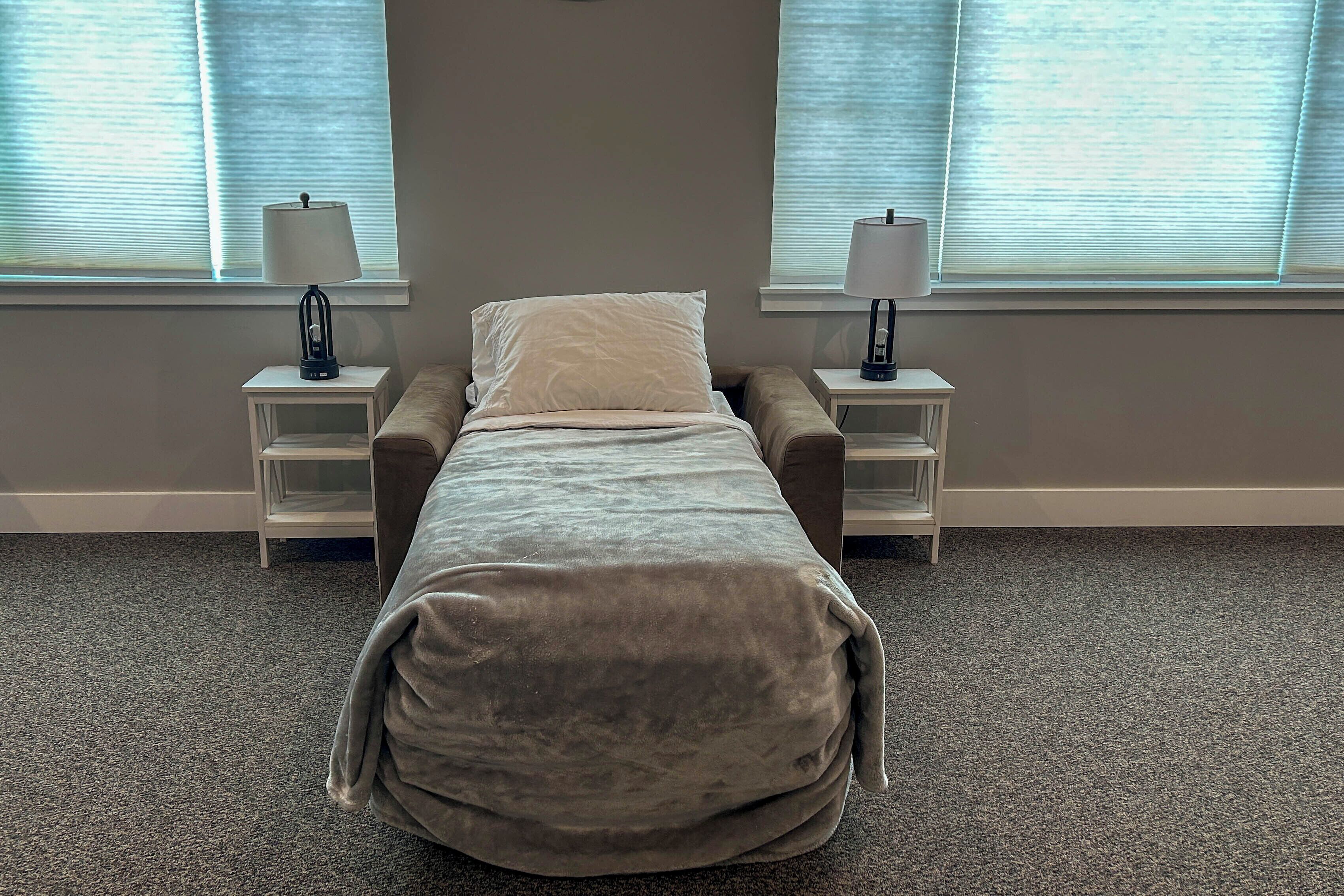 Une chambre avec un lit simple, deux tables de chevet et une fenêtre avec des stores.