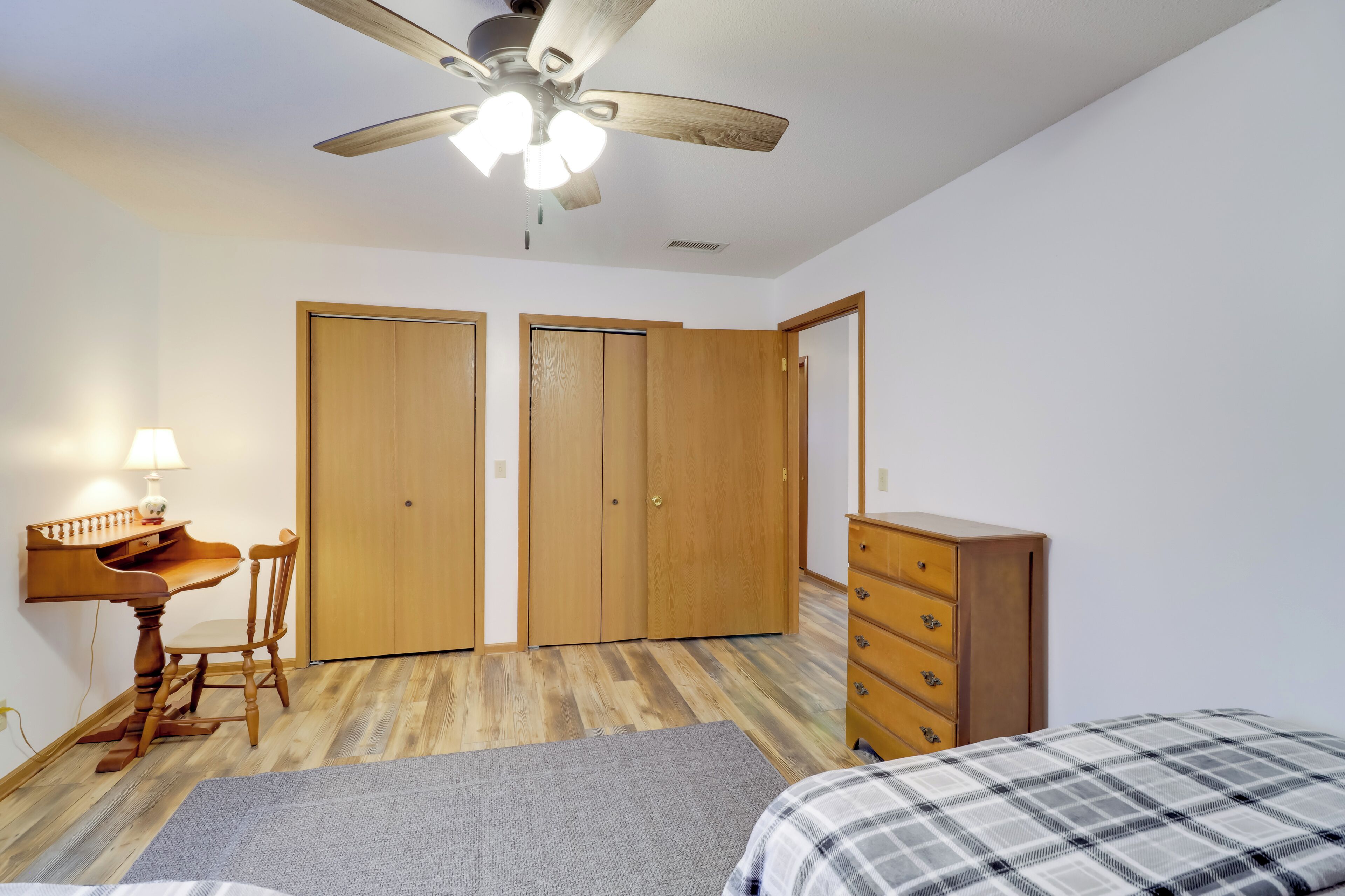 A bedroom with a bed, a desk, a chair, a dresser, and a ceiling fan.