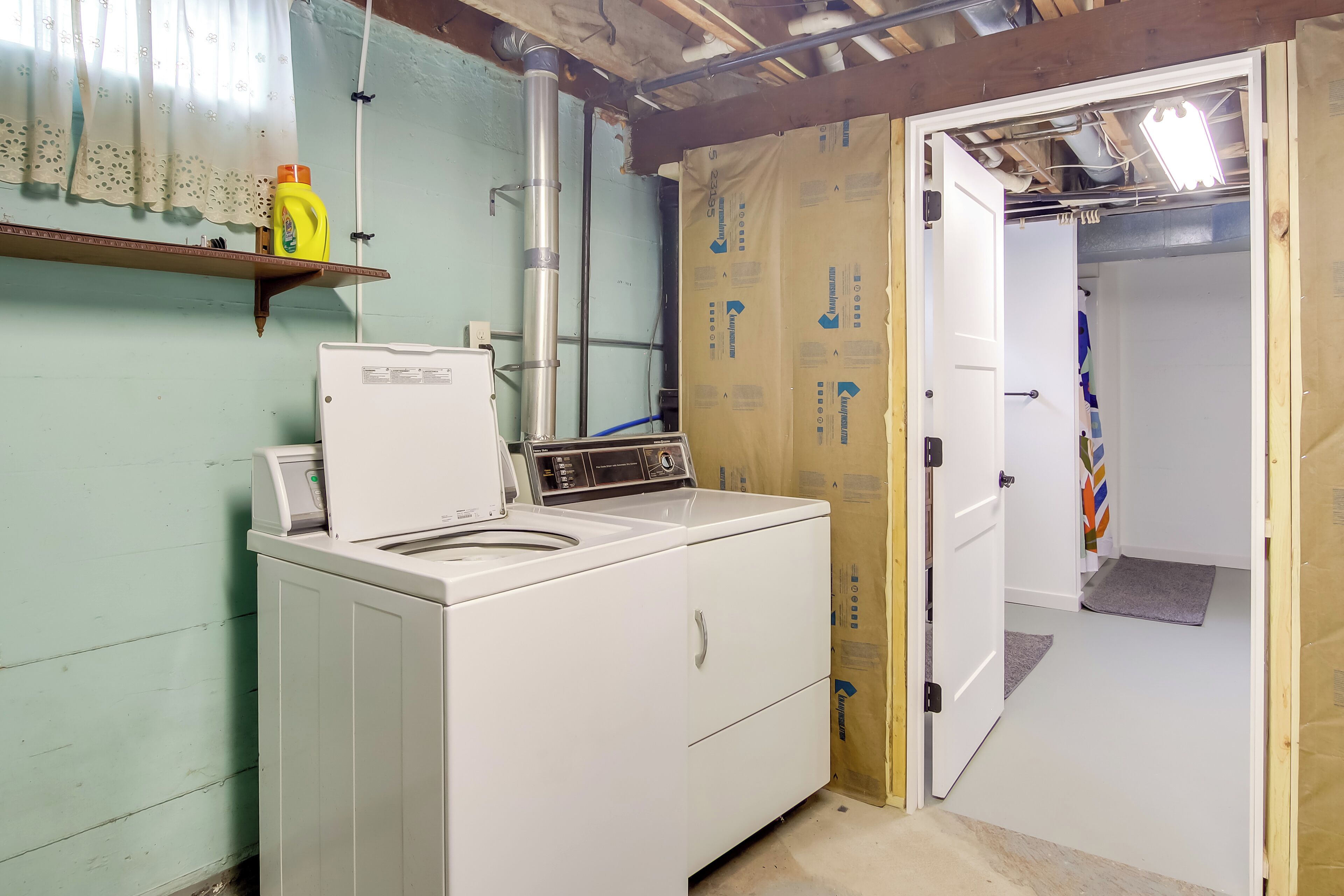 A laundry room with a washing machine and dryer, a shelf with cleaning supplies, and a door leading to another room.