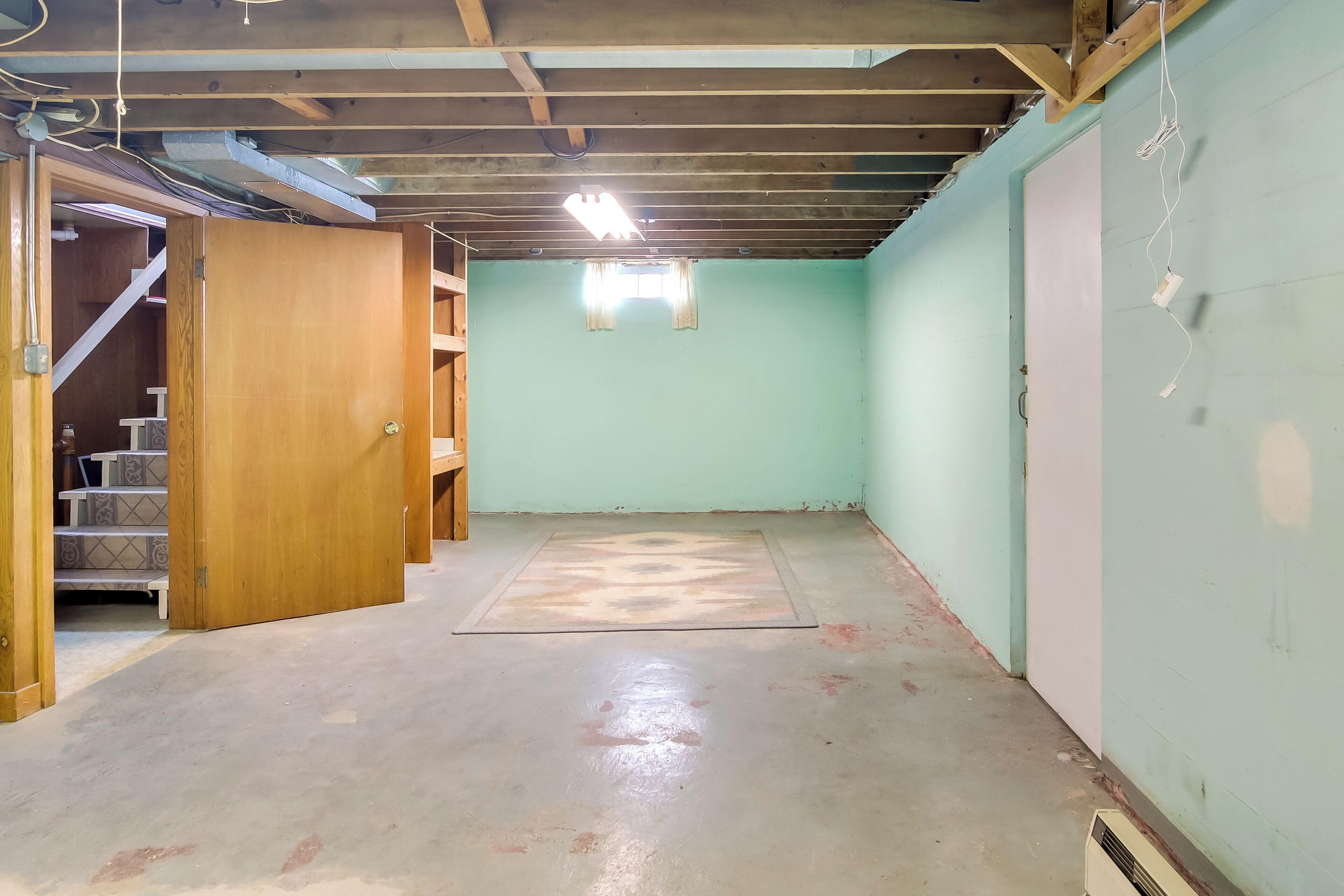 A room with a wooden door, a staircase, a light green wall, and a concrete floor.