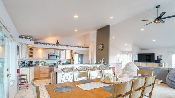 A spacious kitchen with white cabinets, a central island, and a dining area with a wooden table and chairs. - Inviting Great Falls Home w/ Wraparound Deck! (Great Falls)
