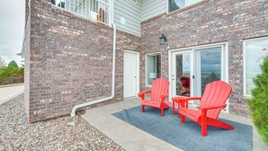 A brick exterior with a covered patio area featuring two red Adirondack chairs and a small table. - Inviting Great Falls Home w/ Wraparound Deck! (Great Falls)