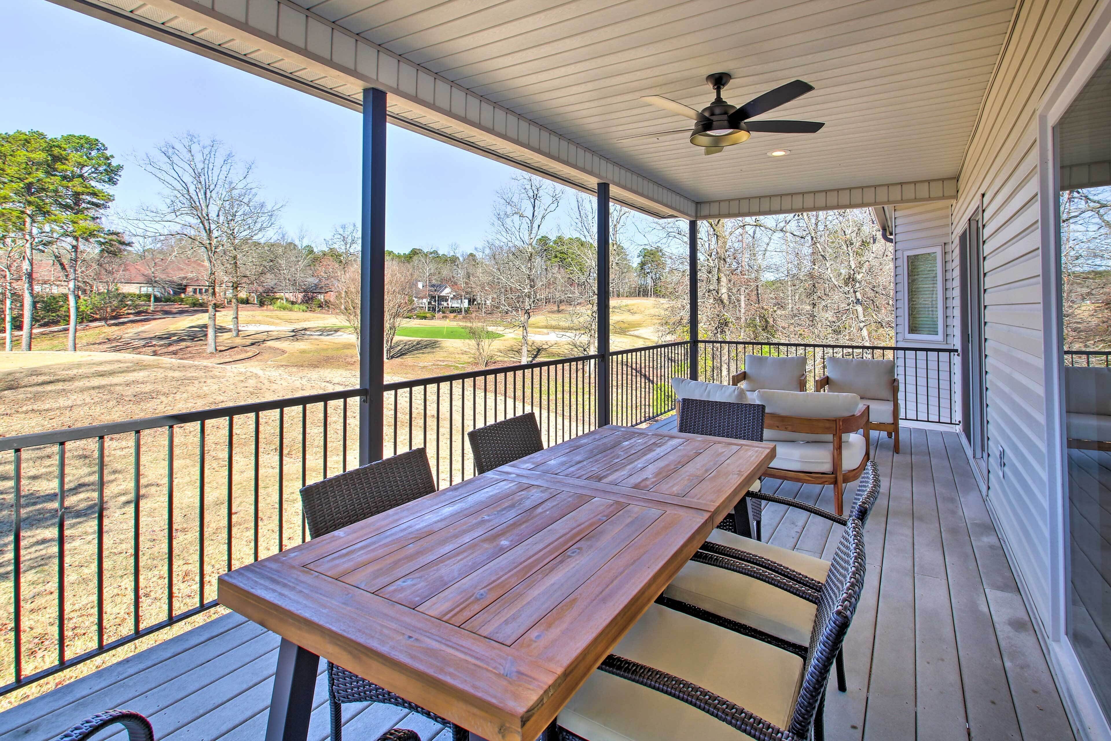 A covered patio with a wooden table and chairs, a ceiling fan, and a view of a golf course.