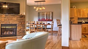 A living room with a stone fireplace, a flat-screen TV, and a dining area with wooden chairs and a table.