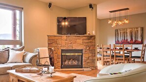 A cozy living room with a stone fireplace, a flat-screen TV, wooden furniture, and a dining area with a table and chairs.