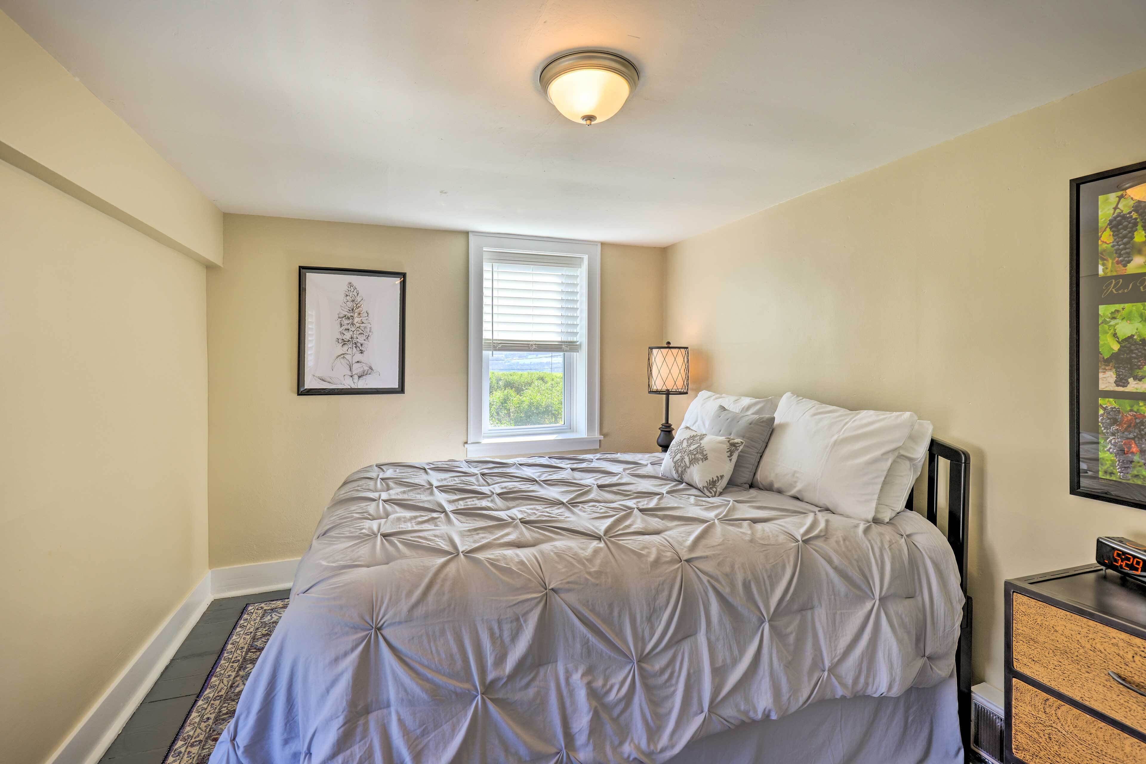 A bedroom with a bed, a nightstand, a lamp, a framed picture, and a window.