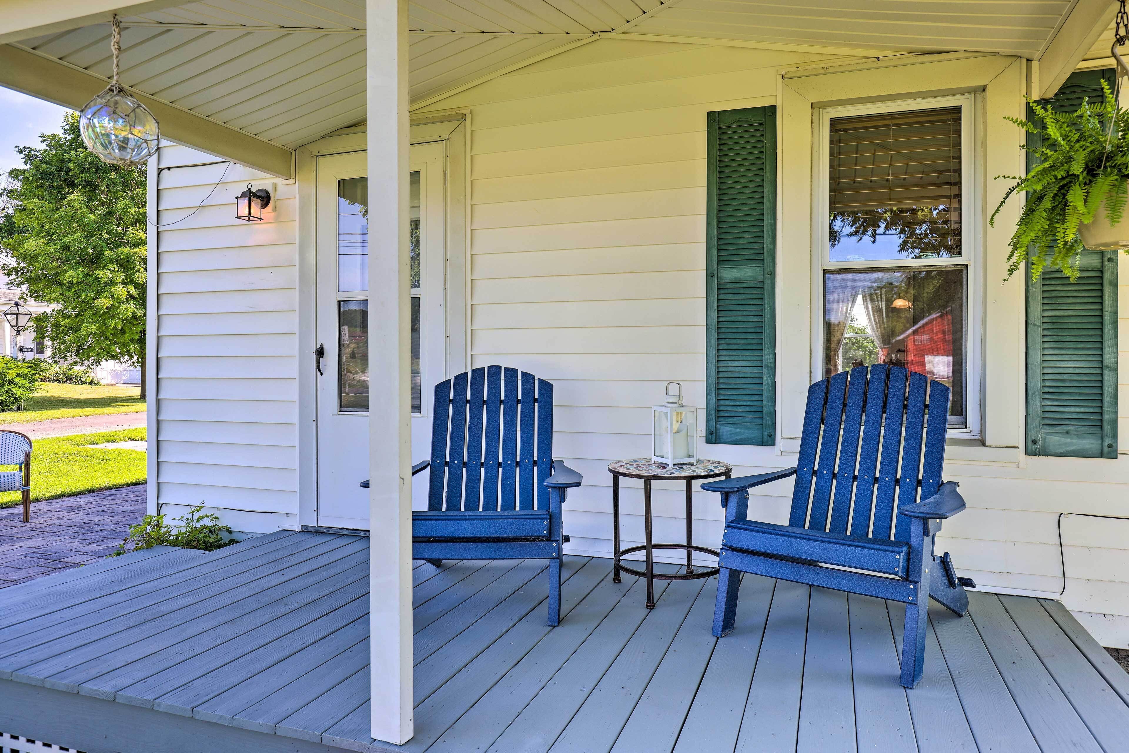 Une véranda avec deux fauteuils Adirondack bleus, une petite table ronde et une lanterne suspendue.