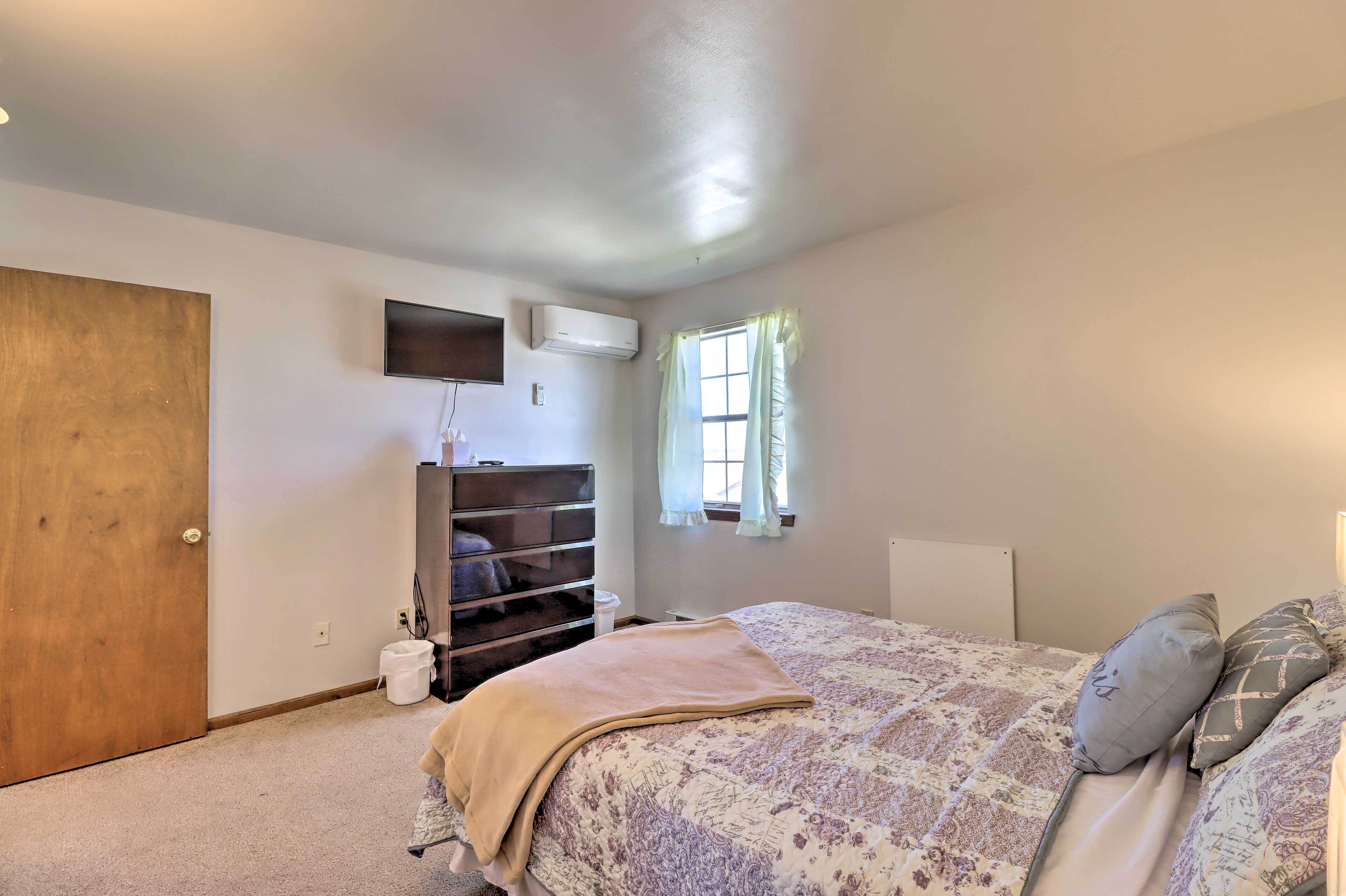 Een slaapkamer met een bed, een dressingkast, een airconditioningapparaat, een raam met gordijnen en een deur.