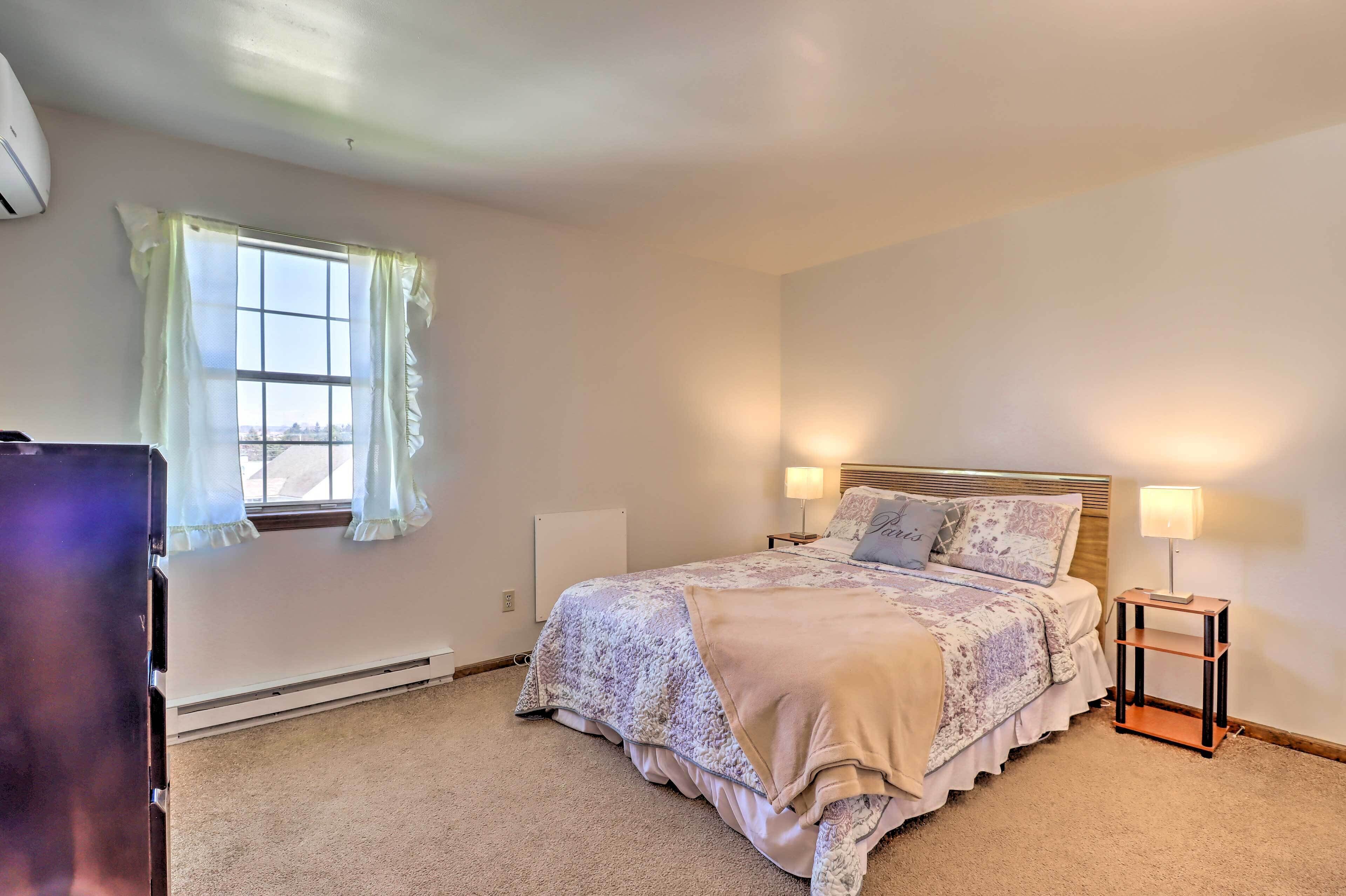 A bedroom with a bed, two bedside lamps, a radiator, and a window with curtains.
