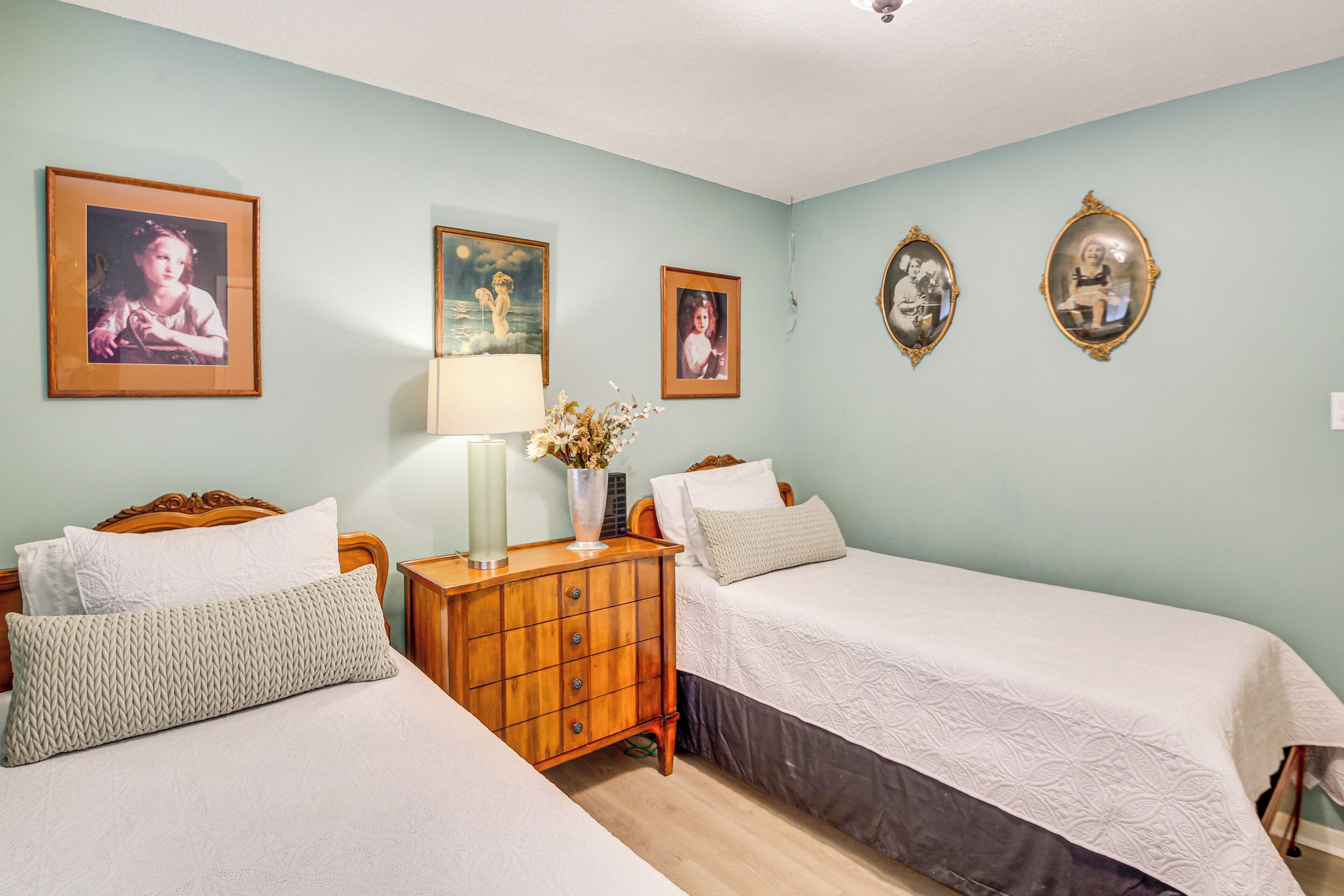 A bedroom with two beds, a nightstand, and wall-mounted pictures.