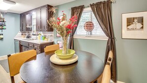 A dining area with a round table, chairs, a vase with flowers, and a window with curtains. - Walk to Bathhouse Row: Dog-friendly Home! (Hot Springs)