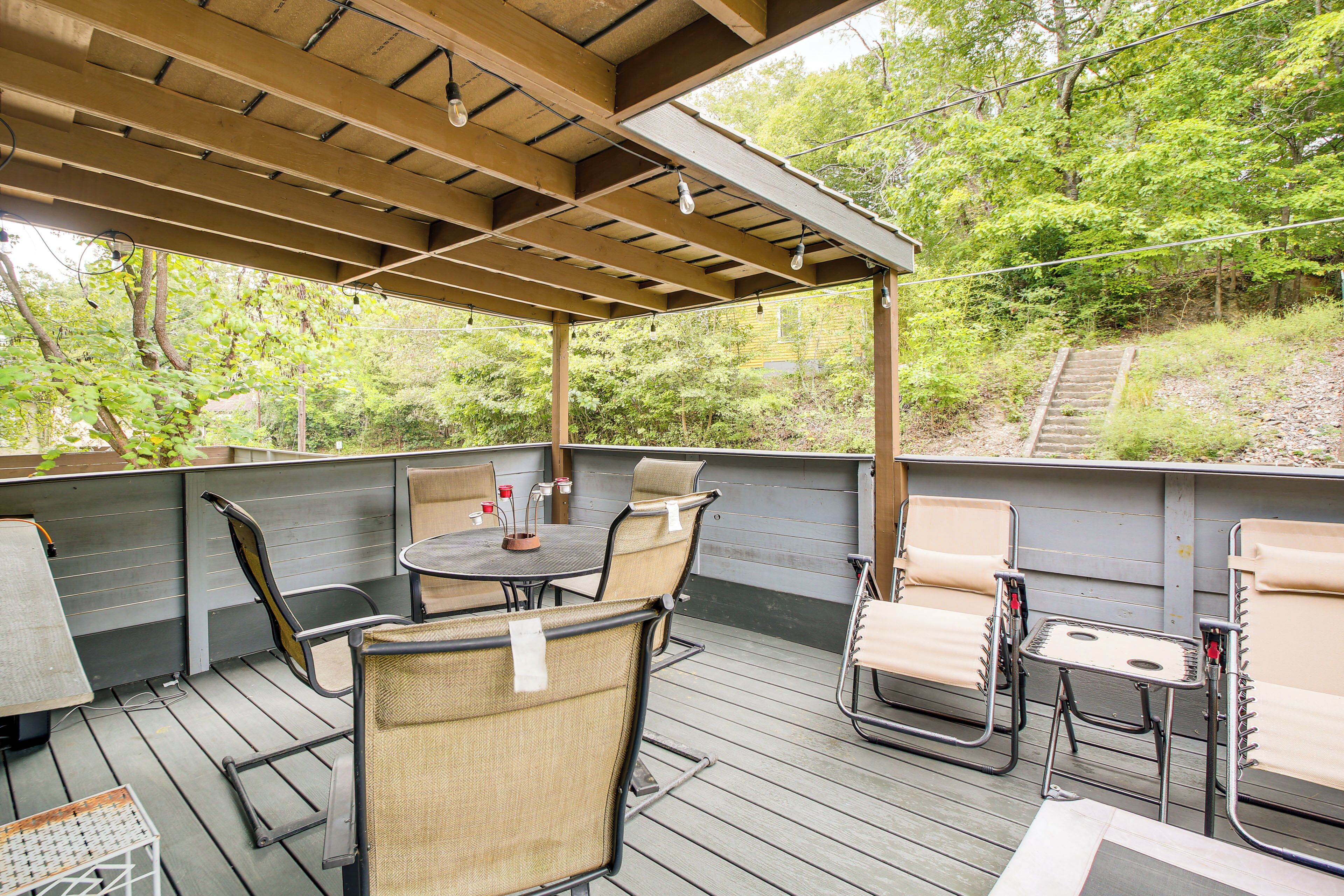 An outdoor patio with a wooden pergola, seating area, and a view of a forested area.