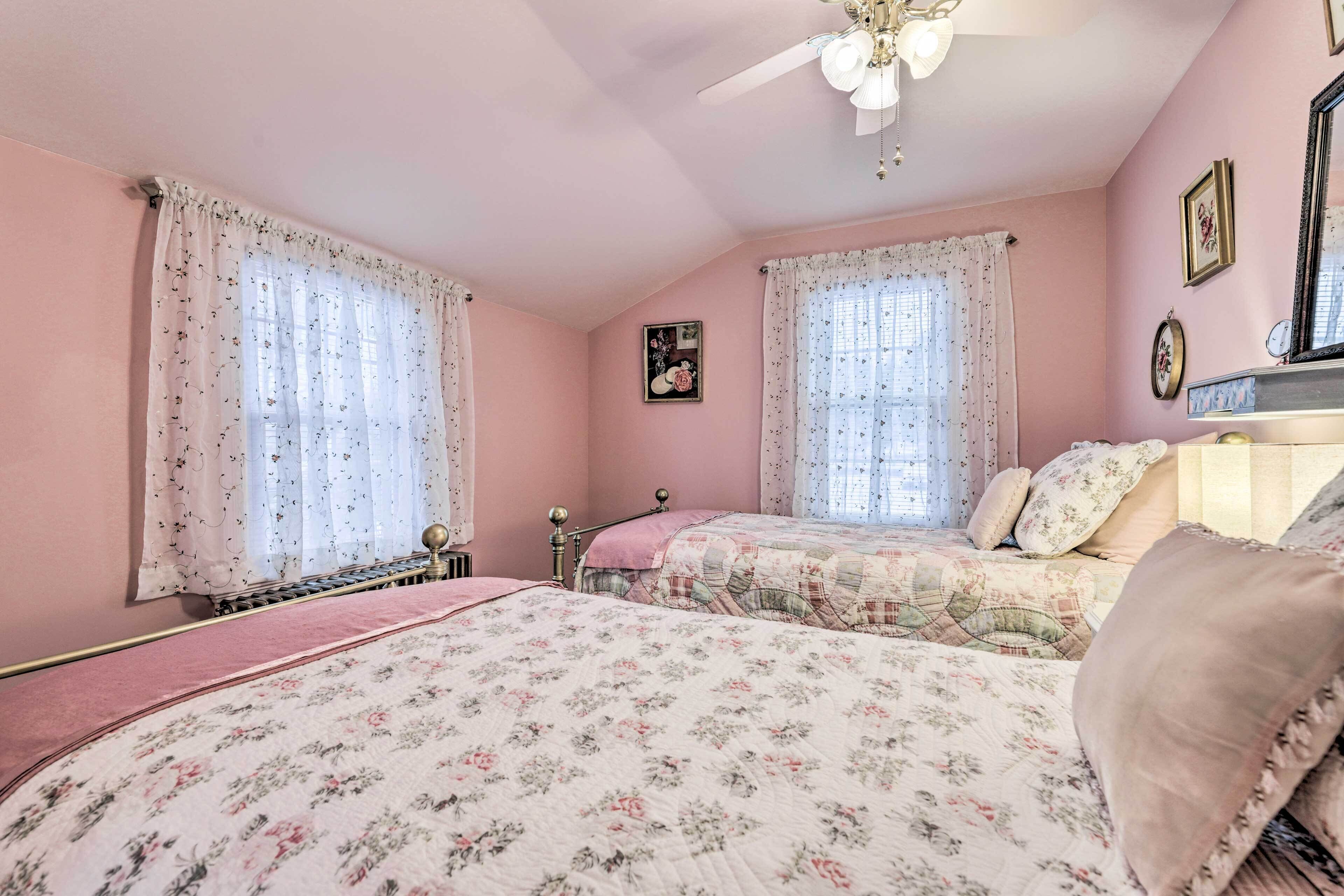 Un dormitori amb decoració rosa, dos llits, roba de llit floral, un ventilador de sostre i un radiador.