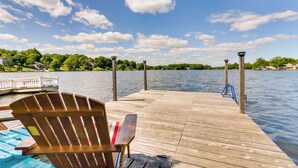 A wooden pier extending into a lake with a wooden chair and a docked boat. - Lakefront Home, Close to Mt Southington! (Wolcott)