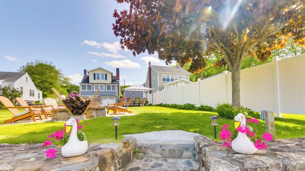 A backyard with a stone wall, a wooden deck, and a white swan statue. - Lakefront Home, Close to Mt Southington! (Wolcott)
