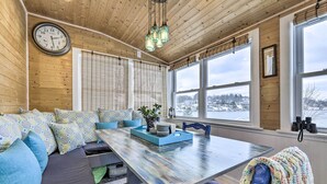 A cozy room with a wooden ceiling, a large window with blinds, a dining table, and a sofa with patterned cushions. - Lakefront Home, Close to Mt Southington! (Wolcott)