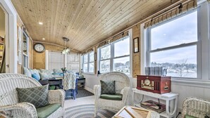 A cozy room with wicker furniture, a clock, and a view of a snowy landscape. - Lakefront Home, Close to Mt Southington! (Wolcott)