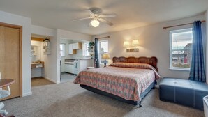 A bedroom with a bed, a ceiling fan, a window with curtains, a bedside table, and a view of the city.