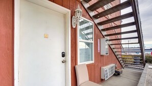 A wooden exterior with a white door, a beige chair, a window, and a staircase.