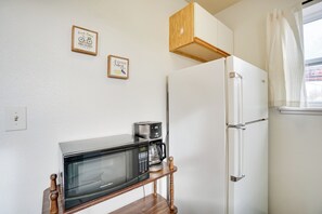 Uma cozinha compacta com micro-ondas, cafeteira e geladeira. Há duas fotos emolduradas na parede.