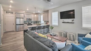 A modern kitchen with white cabinets, a stainless steel refrigerator, and a bar area with stools.