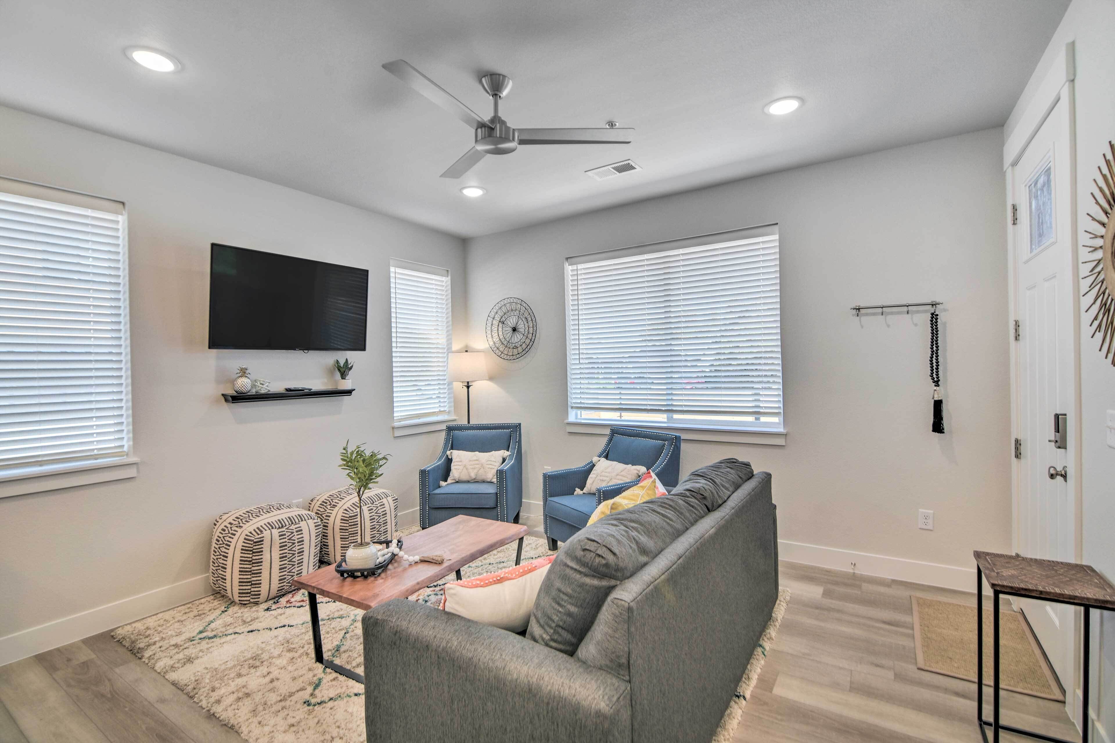 A living room with a gray sofa, two blue armchairs, a coffee table, and a TV mounted on the wall.