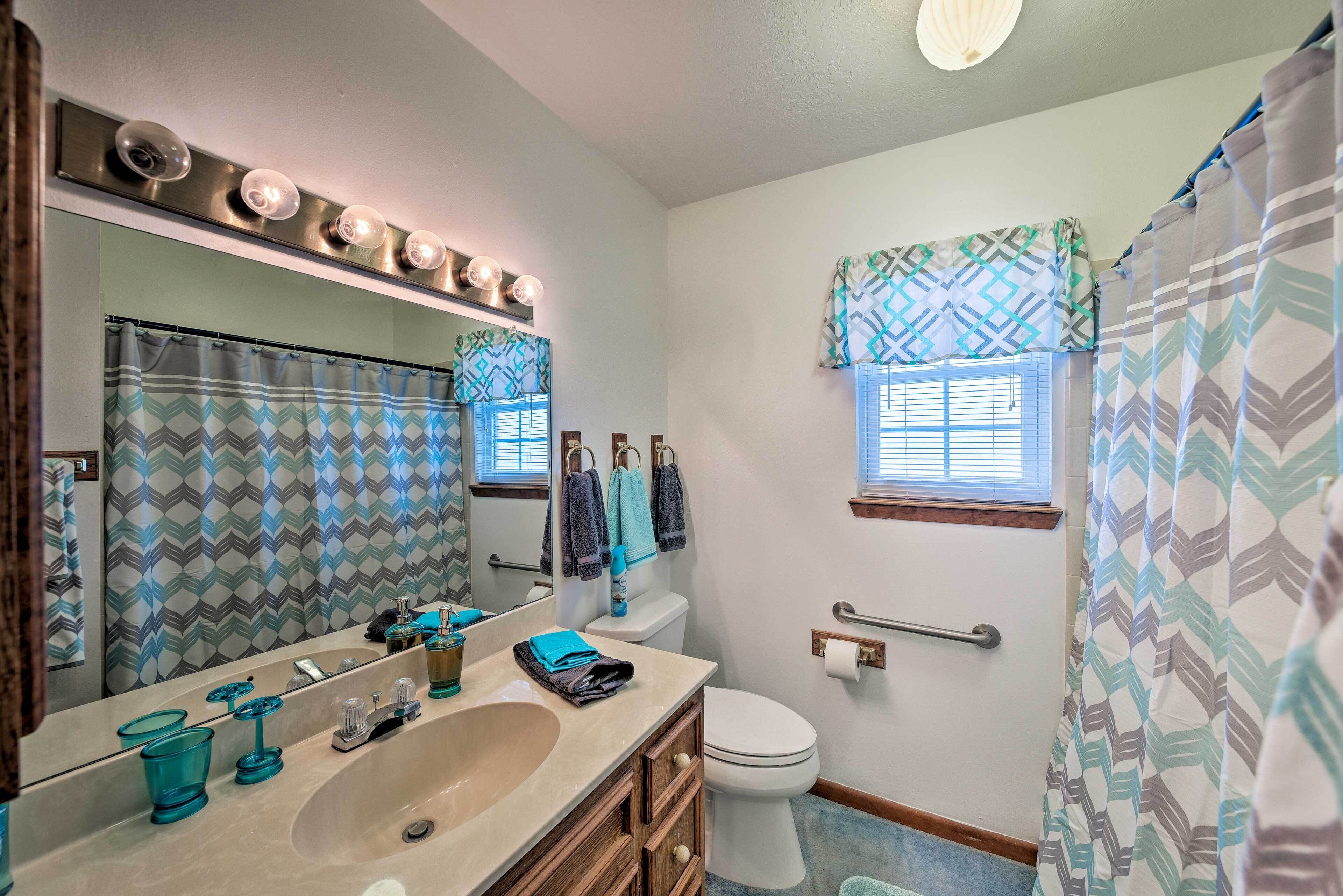 A bathroom with a large mirror, vanity, sink, and toilet. There are patterned shower curtains and a window with blinds.