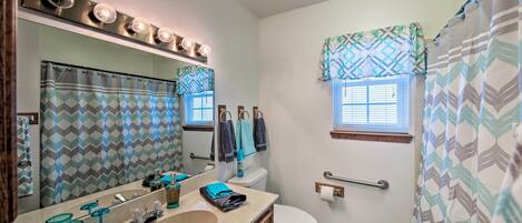A bathroom with a large mirror, vanity, sink, and toilet. There are patterned shower curtains and a window with blinds.